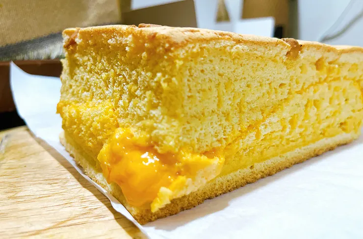 特寫德國起士豆漿蛋糕的側面斷面，淡黃色的綿密蛋糕體中夾著厚實的黃金起士層，層次分明，引發強烈的食慾感。